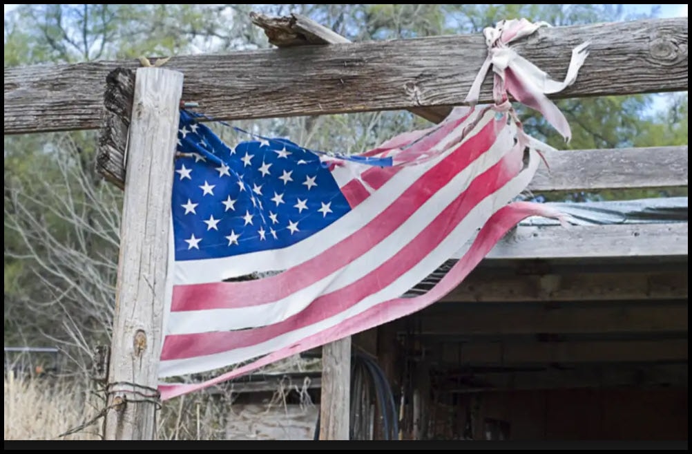 Weathered American flag draped across a rustic wooden fence